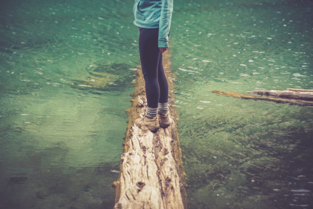 Lower body of person in stretchy pants standing on log in water
