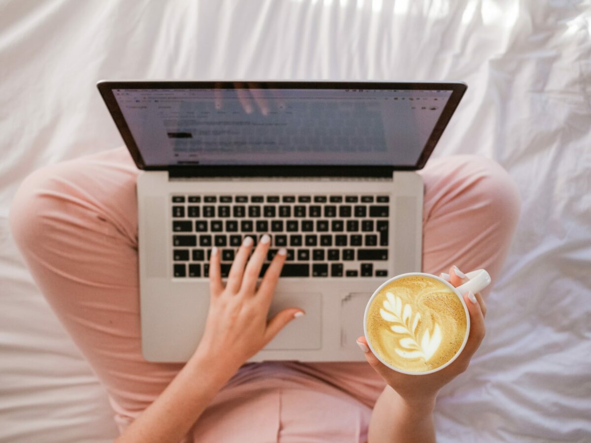 Femme figure in pink pants with a manicure holds a latte and a laptop in her lap
